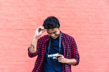 Smiling photographer with vintage camera against red wall. A moment of joy captured in the urban backdrop. Trendy style meets passionate hobby.