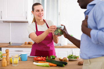 Wife in apron handing food container to husband in kitchen