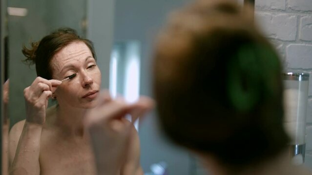 In the cozy atmosphere of her bathroom, an adult woman takes care of her beauty, attaching importance to details and accuracy when using an eyelash comb.