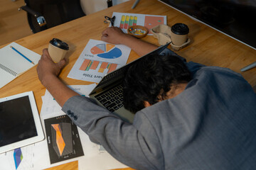 The man who worked hard fell asleep with a cup of coffee at the office.