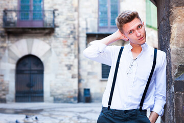 Fototapeta premium Young European guy in shirt and trousers with suspenders walking around city