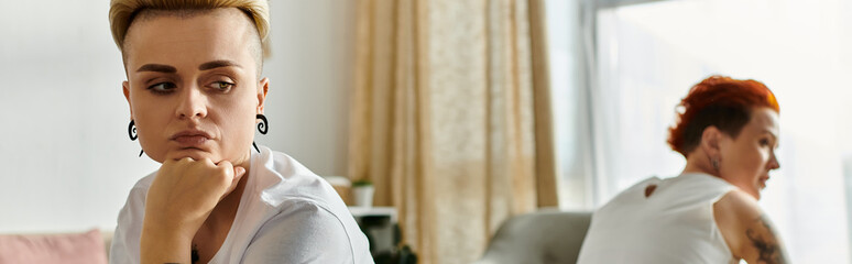 A lesbian couple with short hair sit in a room, facing each other, sharing a deep moment of disconnection.