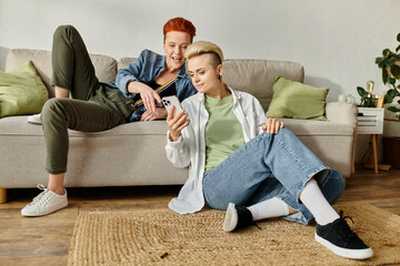 A lesbian couple with short hair sitting on a couch, engrossed in smartphone