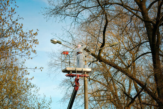 Painter in lift bucket paint street lighting pole at height. Man in disposable paint suit work at height,  painting lamppost with paint brush. Truck crane with utility worker renovate lightning pole