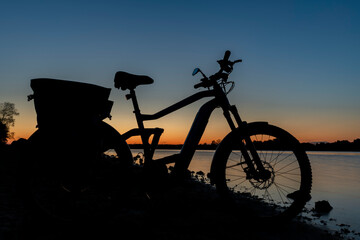 Silhouette of electric bicycle on beach of pond Bezdrev after sunset