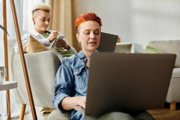 Two women with short hair sitting on a couch, engrossed in a laptop together at home.