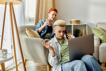 A lesbian couple on a couch using a laptop and talking on the phone.