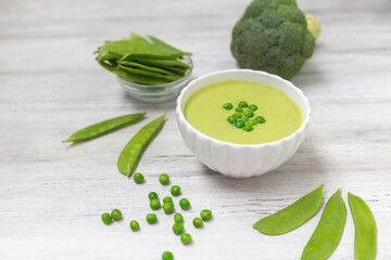 Cream soup with green pea on white wooden background.. 