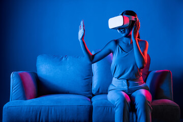 Smart female sitting on sofa wearing VR headset connecting metaverse, future cyberspace community...