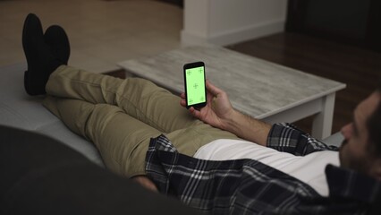 Young man using mobile phone while sitting at home on the sofa using application