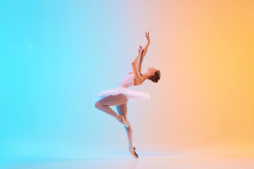 Young ballerina in white tutu dancing and leaning backwards in motion in neon light against...