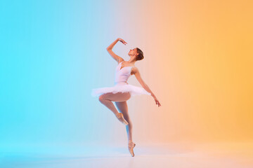 Graceful classic ballerina in white tutu on pointe dancing in motion in neon light against...