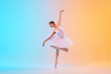 Graceful and poised young ballet dancer performs dance moves in action in neon light against blue-orange gradient background. Concept of art, movement, classical and modern fusion, beauty and fashion