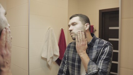 Young man looking in mirror touch his face before shave in bathroom. Slow motion