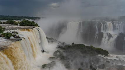 An impressive waterfall landscape. Streams of white foaming water collapse from a ledge in the...