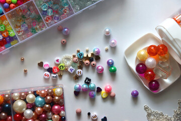 Colorful beads, letter beads, threads and other jewelry making supplies on white background. Making friendship bracelets concept. Flat lay.