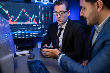 Two stock exchange traders discussing dynamic investment graph in currency rate on monitor at...