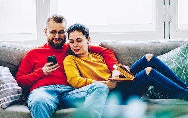 Positive couple in love watching video online on smartphone using wifi connection at home...