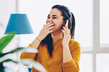 Emotional young woman laughing during mobile phone conversation with friend spending time at home...