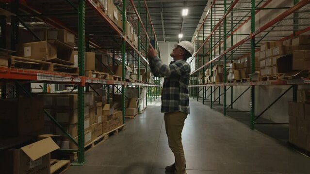 Tracking shot of worker in warehouse checking inventory with scanner / American Fork, Utah, United States