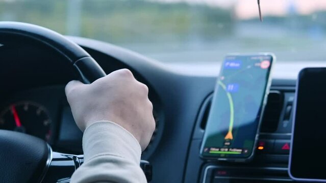 Person drives a car with a cell phone with a navigator on the dashboard.