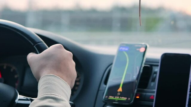 Person drives a car with a cell phone with a navigator on the dashboard.