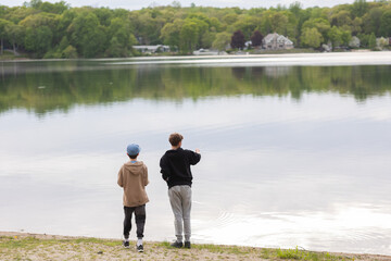 Two adolescent boys look out onto the lake on shoreline at summer sleepaway camp