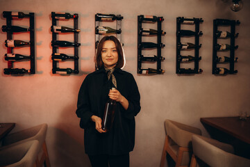 Cheerful caucasian female sommelier opens a bottle of wine with a corkscrew, dressed in classic...