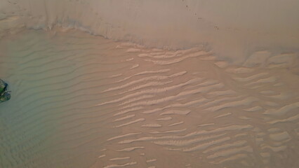 Waves creating rippled texture on sandy beach in aerial. Tranquil tide patterns
