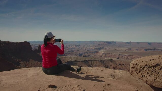 Woman sitting on overlook photographing scenic view at Canyonlands National Park / Utah, United States