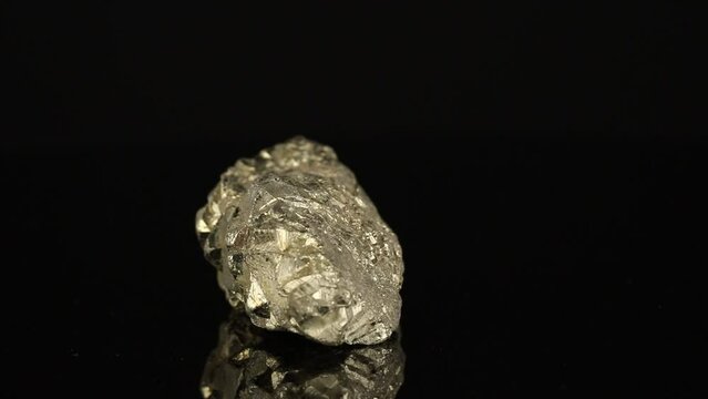 Polished mineral stone pyrite rotates in a circle on a black background