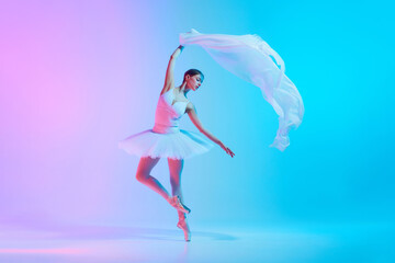 Portrait of young ballerina dancing with light transparent fabric in neon light against vivid...
