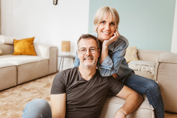 Smiling middle-aged couple spending quality time together in a cozy living room setting, sharing...