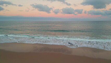 Aerial serene beach sunset view. Waves gently meeting sandy shore in evening