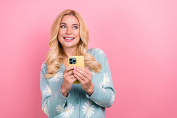 Photo of dreamy woman with wavy hairdo dressed print cardigan hold smartphone look at sale empty space isolated on pink color background