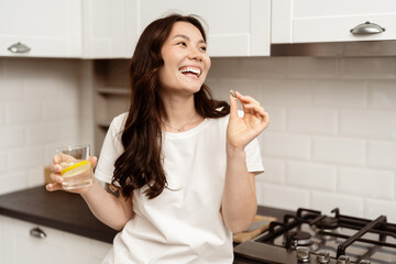 Happy Asian Woman In Kitchen With Vitamin And Water, Showcasing Healthy Lifestyle And Wellness...