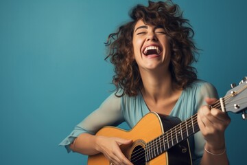 Portrait of a joyful woman in her 30s playing the guitar isolated on soft blue background
