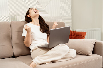 Happy Woman Celebrating Success At Home With Laptop. Joyful Female On Sofa Feeling Excited,...