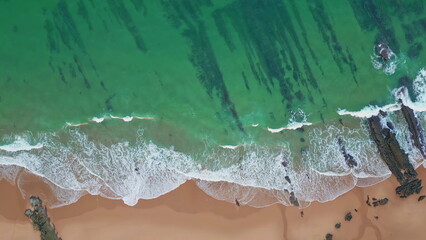 Aerial green sea water crashing sandy beach. Drone view foaming waves caressing