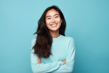 Fototapeta premium Portrait of a joyful asian woman in her 20s with arms crossed on soft blue background