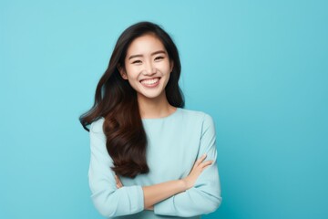 Obraz premium Portrait of a joyful asian woman in her 20s with arms crossed isolated in soft blue background