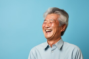 Obraz premium Portrait of a cheerful asian elderly man in his 90s laughing on soft blue background
