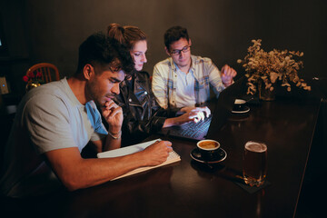 Group of young adults collaborating on a project in a dimly lit cafe in the evening