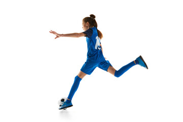 Athletic teen girl in blue uniform in motion, practicing football, kicking ball isolated on white...