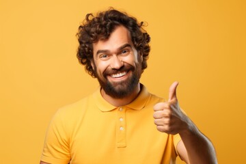 Naklejka premium Portrait of a grinning man in his 30s showing a thumb up isolated on soft yellow background