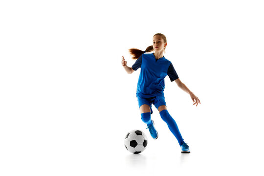 Concentrated teen girl in blue sportswear in motion, playing football, dribbling ball isolated on white studio background. Concept of sport, active and healthy lifestyle, childhood, school, hobby
