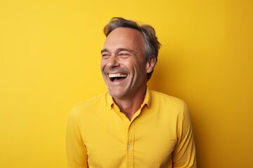 Obraz premium Portrait of a joyful man in his 50s smiling at the camera isolated on soft yellow background
