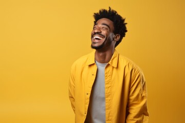 Fototapeta premium Portrait of a glad afro-american man in his 20s laughing while standing against soft yellow background