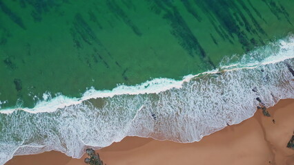 Waves softly crashing beach creating foamy surf. Top view turquoise sea waters