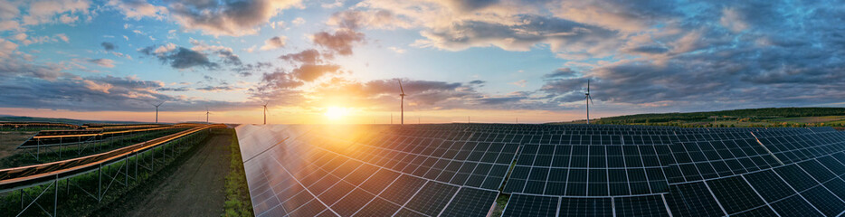 Photovoltaic power station and wind turbines at sunset panorama. Windmill turbines generating green...